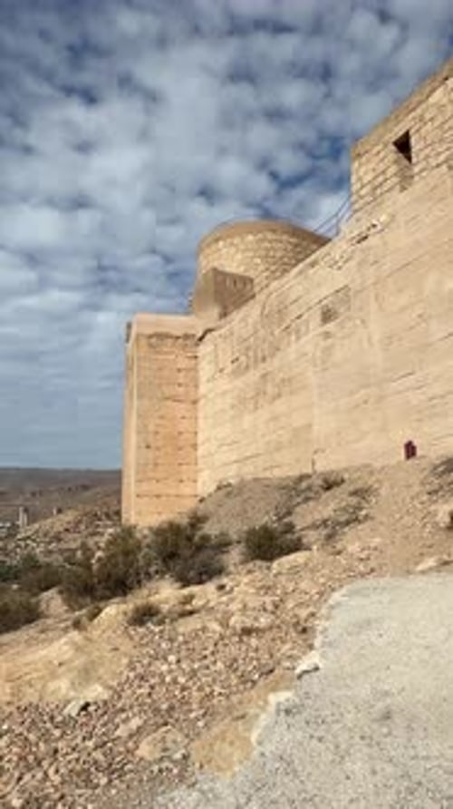 Anciens murs de forteresse en grès s'élevant au-dessus d'un paysage désertique aride sous un ciel nuageux spectaculaire