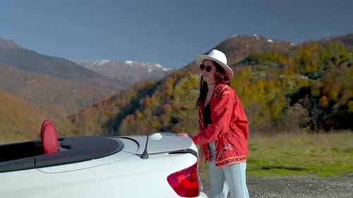 Mujer joven cierra el maletero de un automóvil convertible y se sienta en un automóvil en las montañas