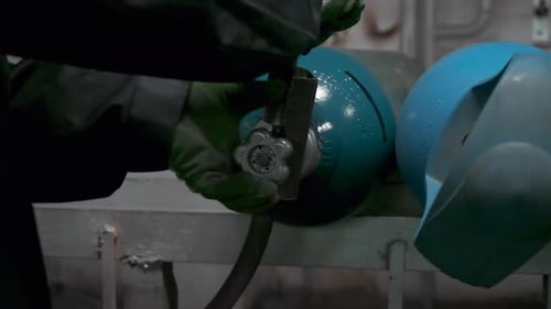 Close up of worker in gloves turning gas cylinder valve. Clip. Industrial background of the factory.