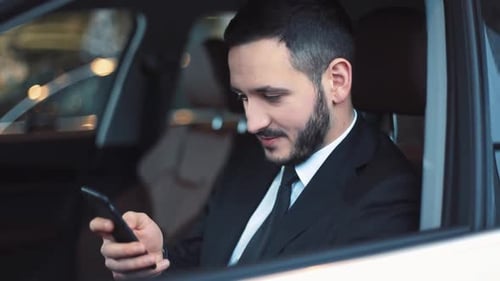 Man in suit using smartphone inside a car