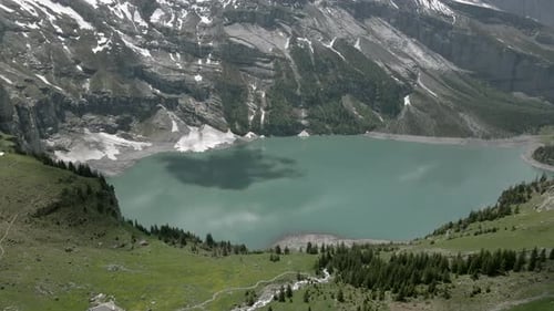 Cloud draws black shadow on the light blue water of the Oeschinensee in the Swiss Alps