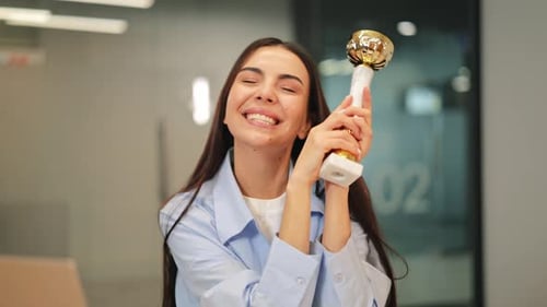 Excited Woman Holding Trophy in Modern Office Setting