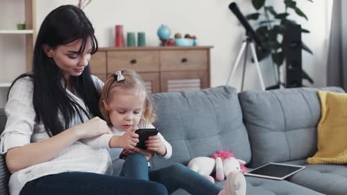 Mother braids hair of child using phone