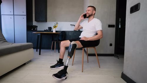 Smiling Man with Prosthetic Leg Talking on Phone in Home Confident Male and His Leg Prosthesis
