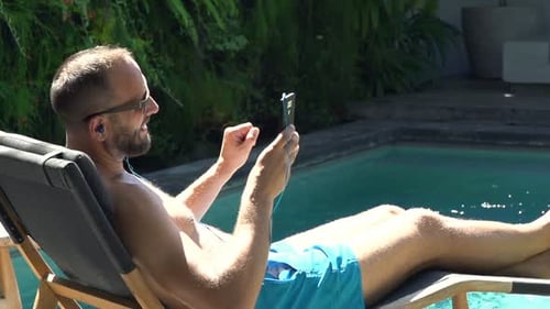 Young Man Listening to Music Lying on Sunbed by Pool Alone