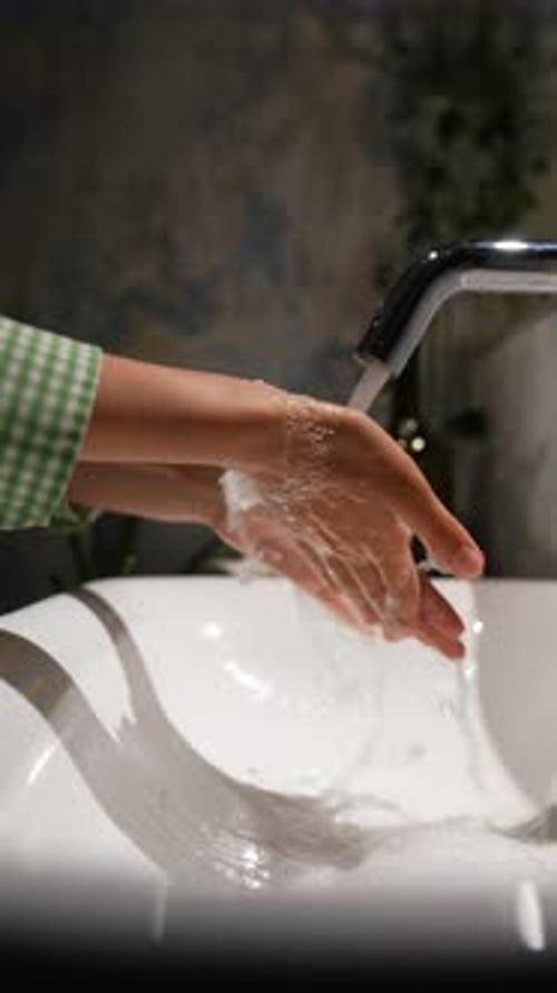 Washing Hands Under Faucet in Bathroom Sink
