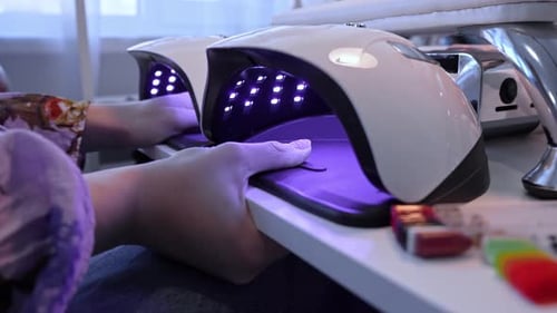 Client places hands into a UV LED nail lamp during a salon manicure, capturing gel polish curing,