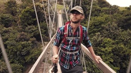 Man Walks Across Suspension Bridge With Lush Greenery