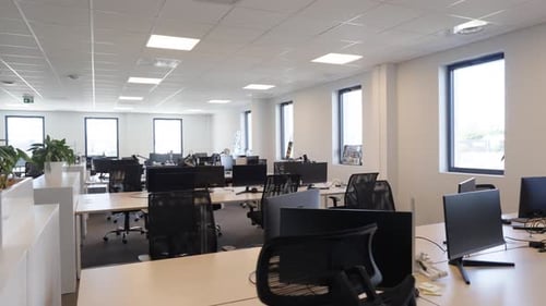 Slow establishing shot of an empty office with laptop screens on desks