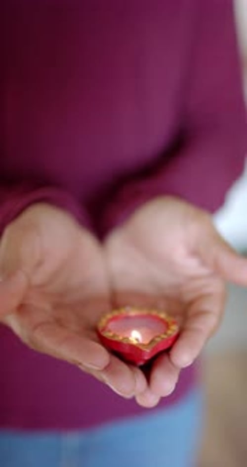 Vidéo verticale : tenant une bougie décorative allumée, personne célébrant le festival indien Diwali à la maison