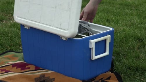 Hombre pasando por una hielera azul en un picnic.