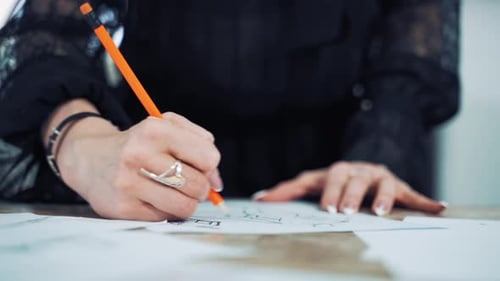 Hands of a professional tailor is drawing a sketch with a sharp pencil on a table.