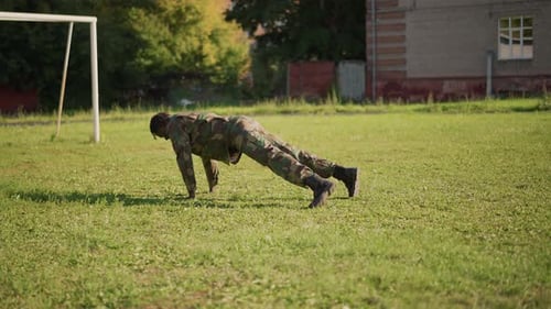 Un soldat termine une série de pompes et se tient debout pour traverser le poteau de but en uniforme camouflage