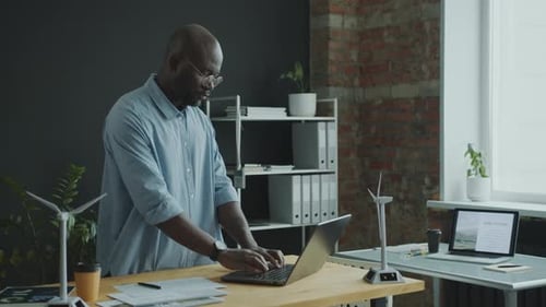 Green Energy Engineer Working on Laptop at Desk in Modern Office
