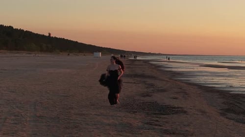 Glückliche schöne Frau in einem langen schwarzen Kleid, das den wunderschönen Sonnenuntergang am Strand in Kalifornien genießt
