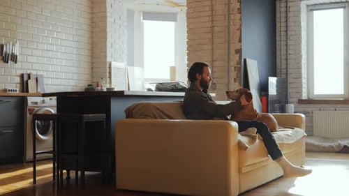 Man Relaxing on Sofa, Petting His Dog