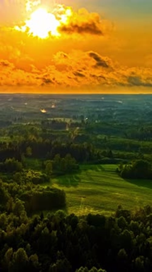 Vue aérienne verticale du soleil doré se levant sur la forêt verdoyante et les champs ruraux en Lettonie