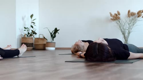 Mujeres en ropa deportiva están tumbadas en el suelo con una colchoneta haciendo yoga en el gimnasio, vista frontal