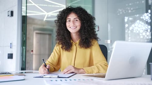 Portrait of young smiling businesswoman sitting at desk at workplace in business office. Happy