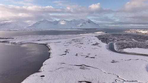 Vista aérea sobre planícies cobertas de neve encontrando as águas geladas de Borgarfjörður perto de Borgarnes