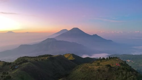 Aerial view of lush greenery mountain ridge at sunrise with dramatic sky and volcanic peaks