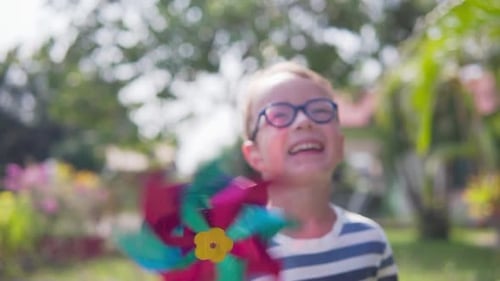 Boy in glasses is playing with pinwheel in a garden