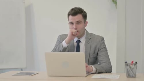 Man Coughs While Working at Laptop in Office