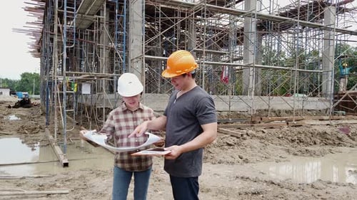 Construction manager and engineer discussing and checking plans on construction site.