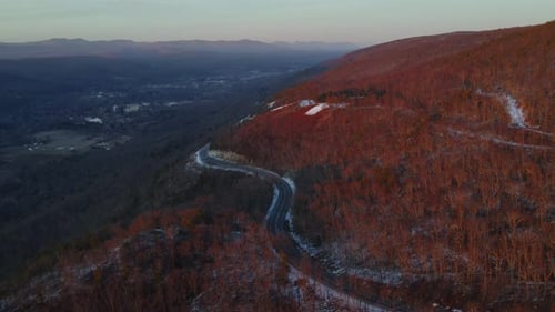 En survolant une route panoramique sur une montagne surplombant une vaste vallée en hiver, juste après le coucher du soleil,