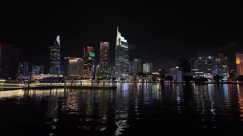 A breathtaking nighttime cityscape featuring illuminated skyscrapers reflecting on a calm river. The