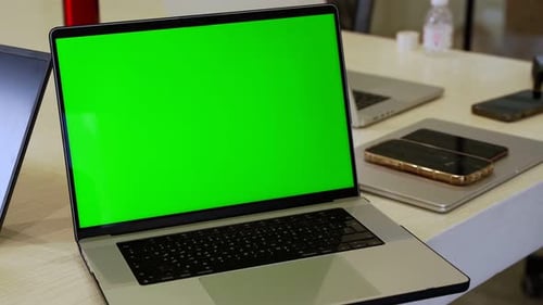 Laptop with Green Screen in Office with Phones and Gadgets on Desk
