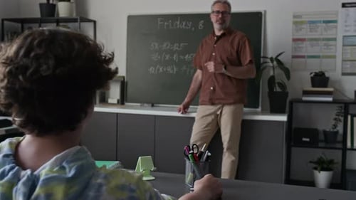 Mature Male Teacher Explaining Math to Teenage Boy Raising Hand