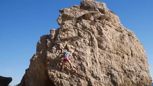 Man climbing tall rock on beach.