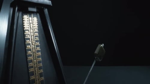 Dolly out shot of a vintage black metronome swinging back and forth