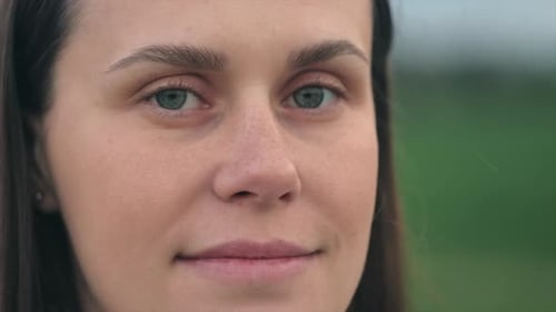 Close up portrait of attractive young caucasian woman standing in field, looking at camera