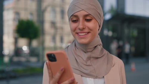 Smiling Woman in Headscarf Using Smartphone Outdoors
