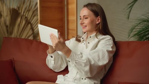Woman Smiling Using Tablet on Couch Indoors