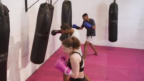 Diverse trainees guarding before heavy bags at gym, delivering jab-cross-hook drills for speed