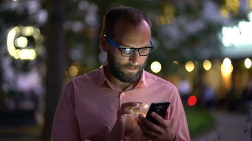 Man Texting, Sending Sms on Smartphone at Night in the City 30s