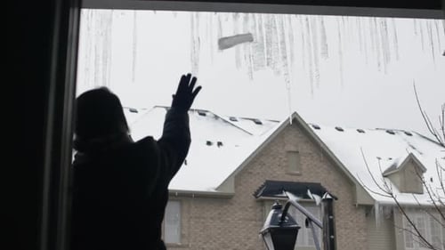 Woman knocks icicles off gutters in slow motion by throwing a piece of ice