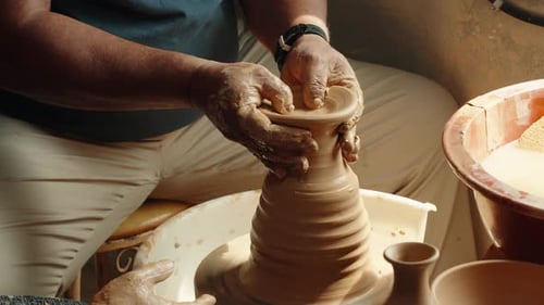 Close-Up of Hands Shaping Tall Clay Vase on Pottery Wheel in Warm Studio Light