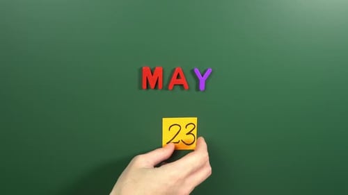 Hand sticking a sticker 23 May calendar day on school board. 23 date of May. Twenty third day