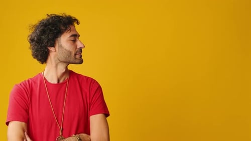 Smiling man points to side to show advertising space isolated on yellow background in studio