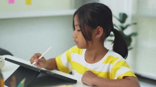 A girl drawing on tablet using stylus at table, leading dad working on laptop.
