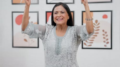 Woman Celebrates Good News, Posing Indoors with Arms Up