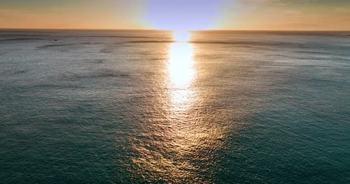 Sunset over the vast waterscape of the ocean. Aerial perspective on the water reflecting the sun.