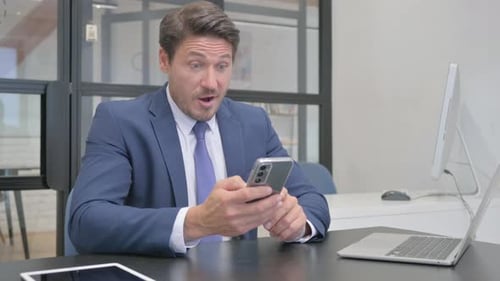 Excited Businessman Celebrates Good News on Phone in Office