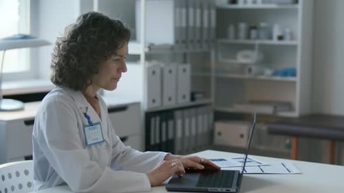 Female Doctor Working on Laptop at Desk in Medical Office