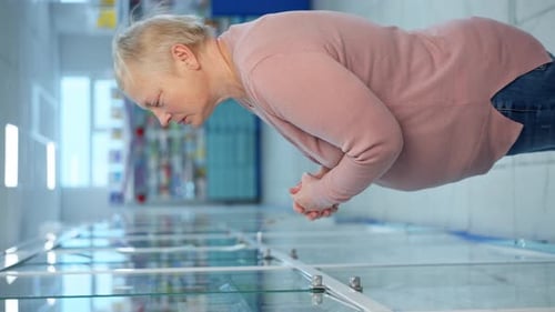An Elderly Woman Looks at the Shelves with Goods in a Pharmacy