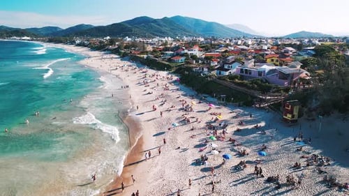 Aerial view of the sea with gentle waves and sandy beach with people relaxing on it